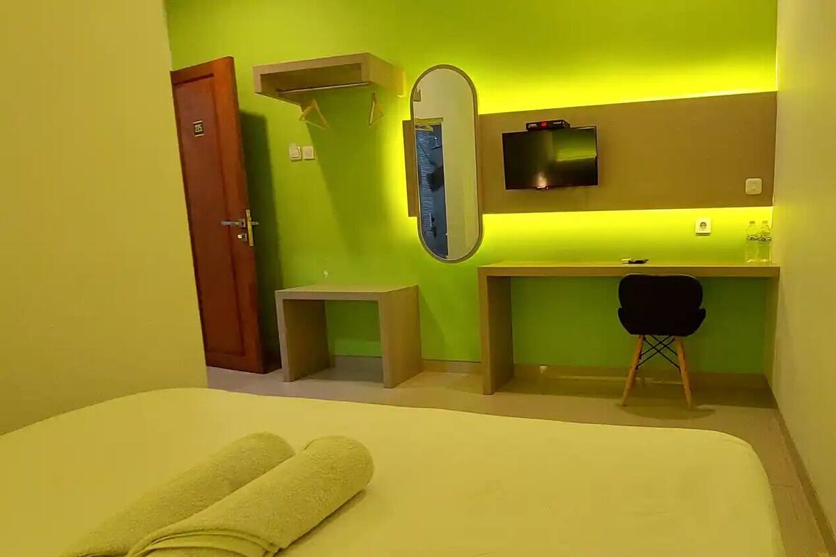 Una habitación de hotel con cama, escritorio, silla, televisor y espejo.
