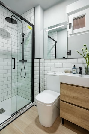 Ein modernes Badezimmer mit einer Duschkabine aus Glas, einer weißen Toilette, einem Holzausleger und einem Spiegel über dem Waschbecken.
