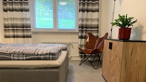 Makuuhuone, jossa on sänky, puinen kaappi, tuoli ja ruukkukasvi.