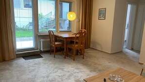 Huone, jossa on ruokapöytä, tuoleja, patteri, ikkuna, jossa on s älekaihtimet, taulu seinällä ja ovi, joka johtaa toiseen huoneeseen.