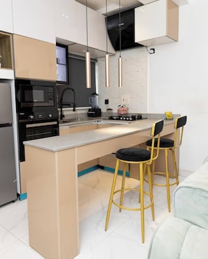 A modern kitchen with a central island, bar stools, a microwave, oven, and a gas stove.