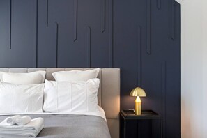 Una cama bien hecha con almohadas, una mesita de noche con lámpara y una pared con diseño geométrico.