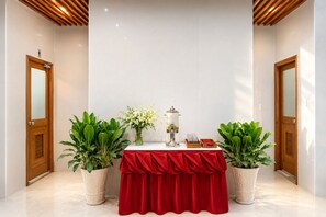 Ein Empfangsbereich mit rotem Tisch, Topfpflanzen, Wasserspender und Spiegel an der Wand.