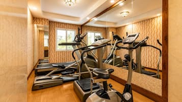 Un gimnasio con cintas de correr, bicicletas estáticas y un espejo grande.