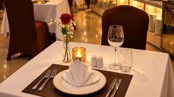 A dining table set with a white tablecloth, a vase with a red rose, salt and pepper shakers, a candle, and a wine glass.
