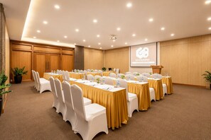 Une salle de conférence équipée de plusieurs tables et chaises, d’un écran de projection et d’un pupitre.