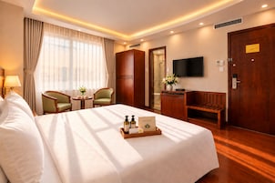 A hotel room with a bed, a desk, a chair, a television, and a wardrobe.