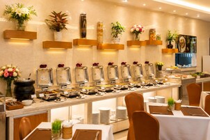 A buffet setup with various food stations, a wall-mounted plant display, and a dining area with tables and chairs.