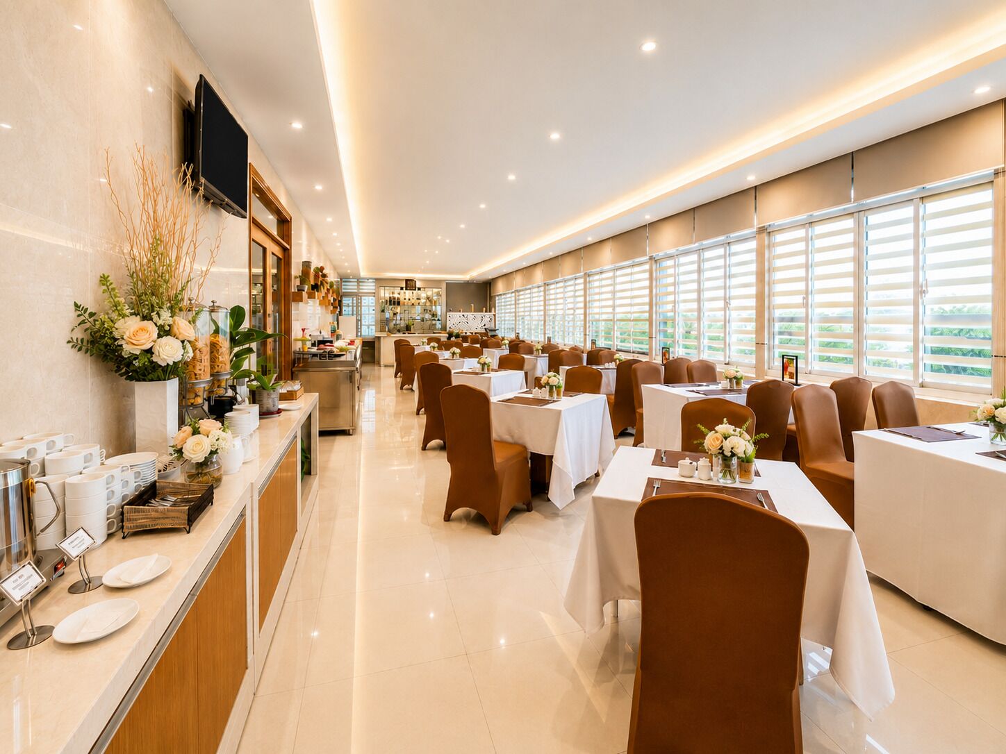 A restaurant with multiple tables and chairs, a counter with a coffee machine, and a TV mounted on the wall.