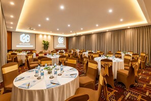 Une salle de conférence équipée de plusieurs tables rondes, chacune étant pourvue de chaises et de tout le nécessaire, notamment des bouteilles d’eau et des documents.