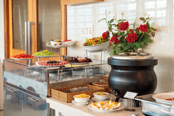 A buffet setup with various food items, a hot pot station, and a floral arrangement.