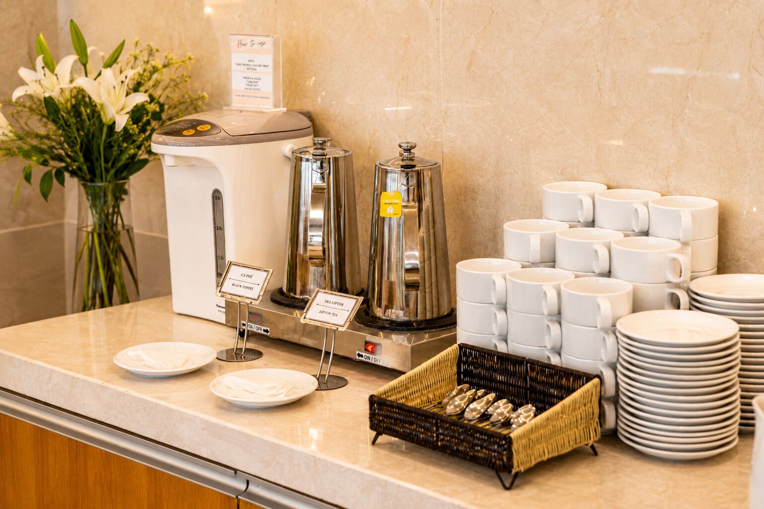 A buffet setup with coffee machines, tea dispensers, and a variety of white mugs and plates.