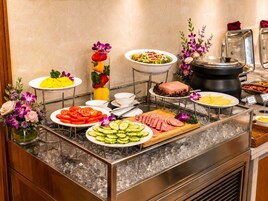 A buffet with various food items, including sliced tomatoes, cucumbers, and meats, along with a selection of beverages and a decorative flower arrangement.