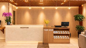 A reception desk with a wooden finish, a tour desk with brochures, and a potted plant.