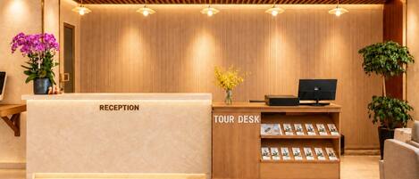 A reception desk with a wooden finish, a tour desk with brochures, and a potted plant.