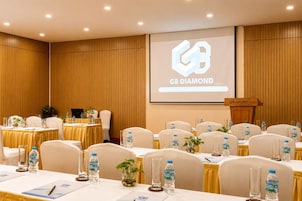 Ein Konferenzraum mit für eine Besprechung gedeckten Tischen, einem Rednerpult und einer Projektionsleinwand, die 'G8 DIAMOND Hotel and Convention Center' zeigt.