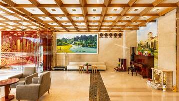 A hotel lobby with a modern design, featuring a large painting of a landscape, a piano, and a seating area with sofas and a coffee table.