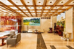Eine Hotellobby im modernen Design, mit einem großen Landschaftsgemälde, einem Klavier und einer Sitzecke mit Sofas und einem Couchtisch.