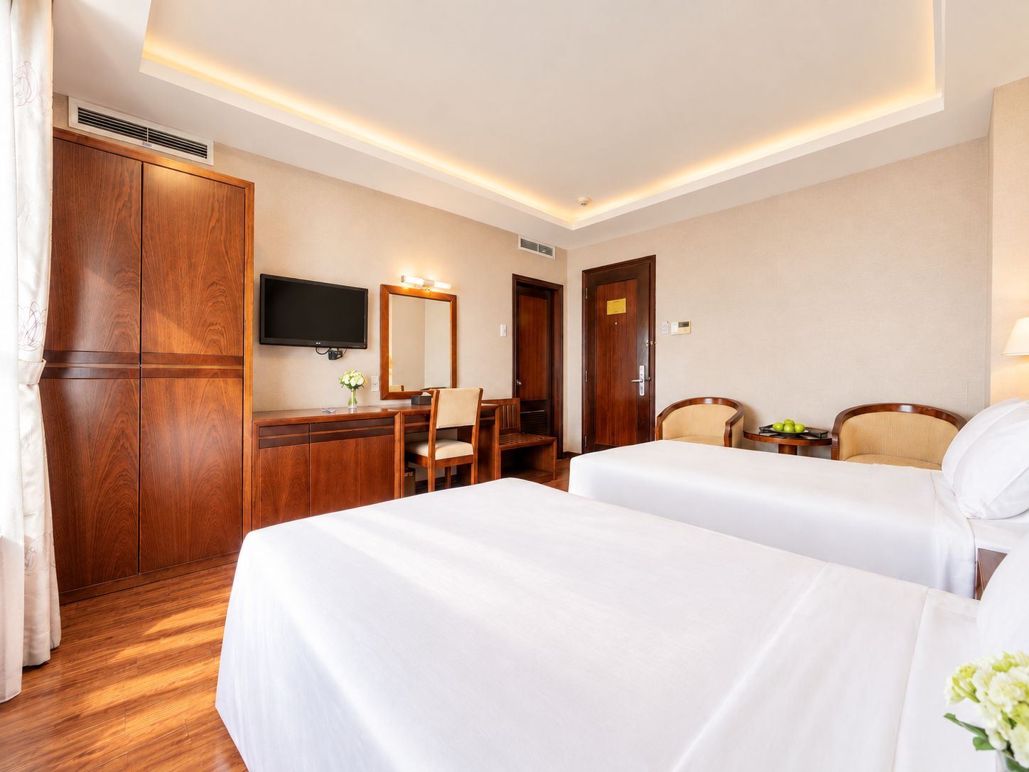 A hotel room with two beds, a desk with a chair, a television, and a wardrobe.