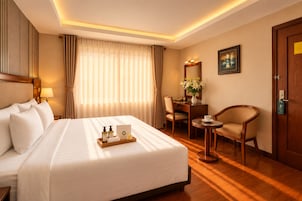 A hotel room with a large bed, a desk, a chair, a small table, and a door.