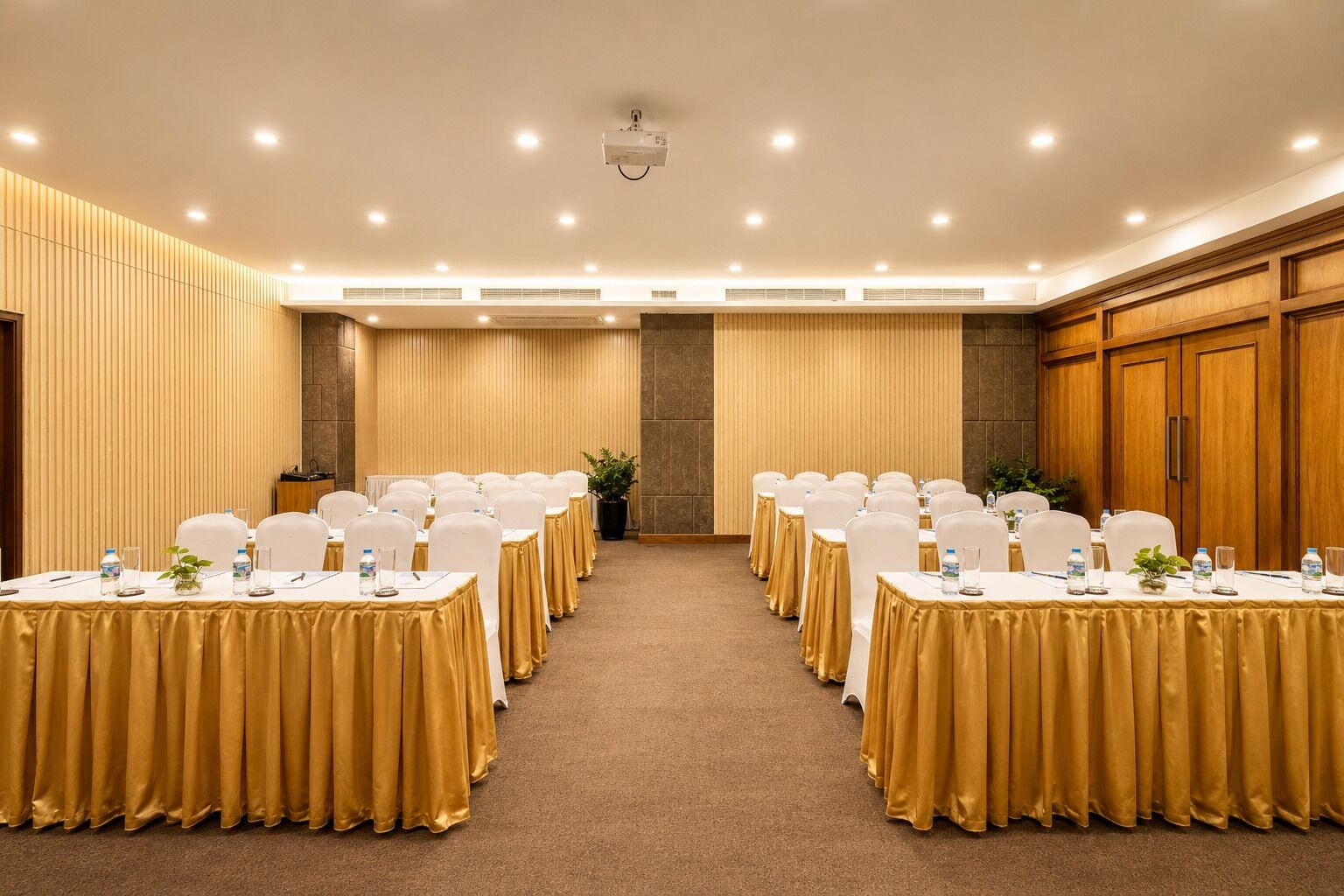 A conference room with rows of tables, each with a white tablecloth and chairs, and a carpeted floor.