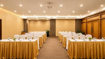 A conference room with rows of tables, each with a white tablecloth and chairs, and a carpeted floor.