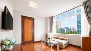 Un salon moderne avec un canapé, une table basse en verre, un téléviseur et une vue sur la ville.