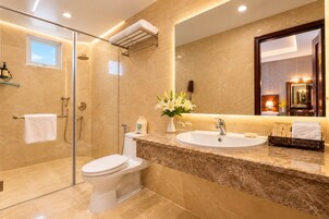 Une salle de bain moderne avec une douche à parois de verre, des toilettes blanches, un comptoir en marbre, un lavabo et un grand miroir.