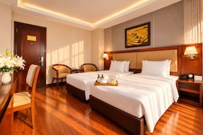 A hotel room with two beds, a desk, chairs, a painting, and a nightstand with a lamp. - G8 Diamond Hotel Saigon (Ho Chi Minh City)
