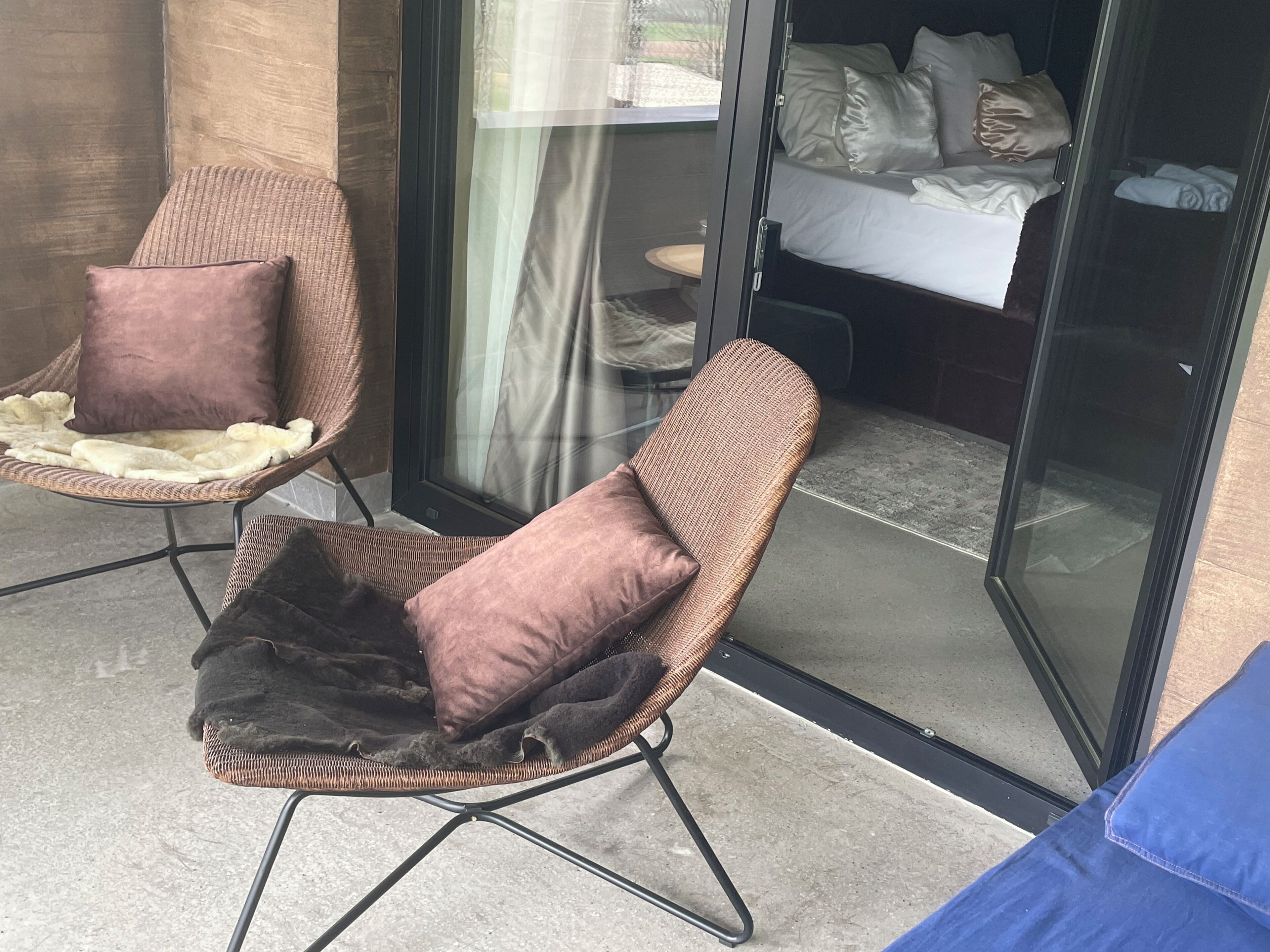 A room with a bed, a glass door, and two wicker chairs with cushions.