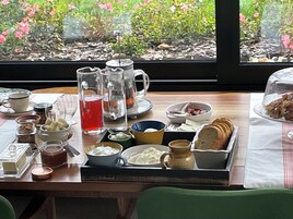 Una mesa de desayuno con diversos alimentos, una jarra y vista a zonas verdes a través de una ventana.