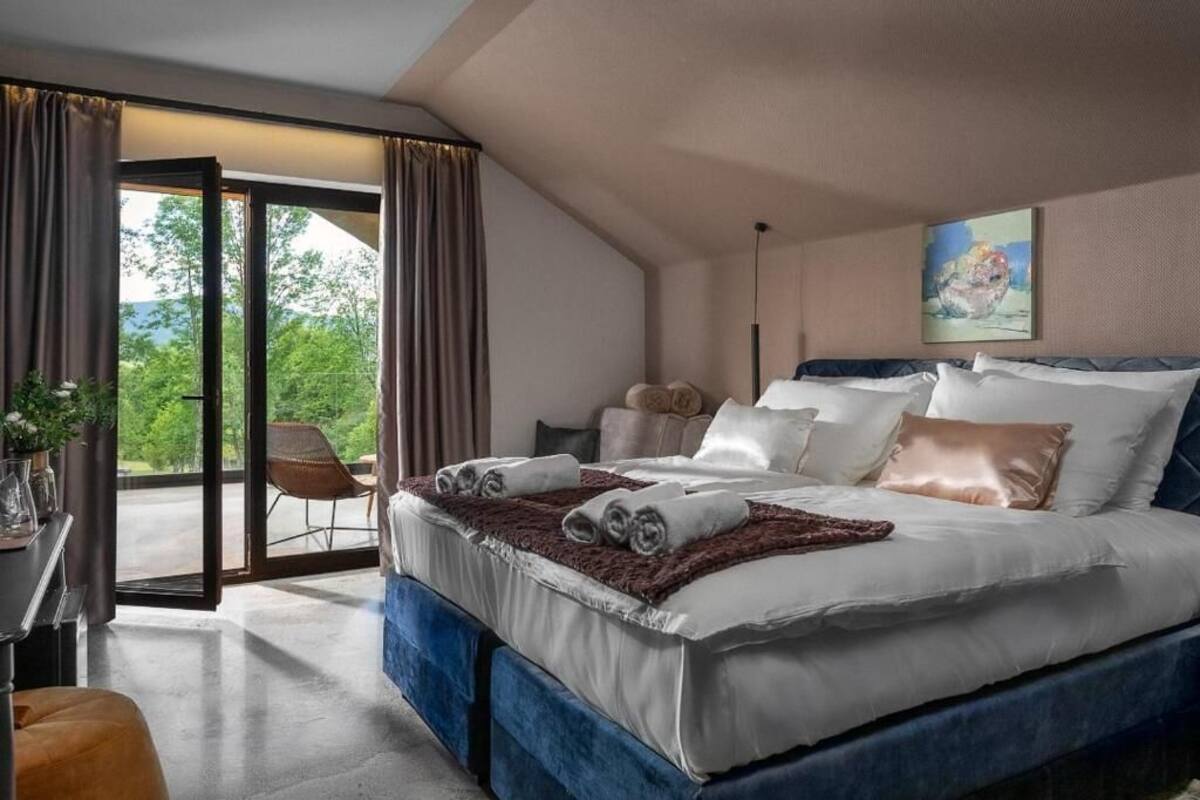 A bedroom with a large bed, a chair, a desk, and a view through a glass door.
