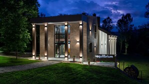 Un edificio moderno con fachada de vidrio, iluminado por luces exteriores, y un letrero que dice 'equilibrium'.