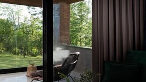 A modern living room with a green sofa, a wooden coffee table with a vase, and a view of a green lawn through large windows. - Equilibrium Villa Relais Plitvice (Rakovica)