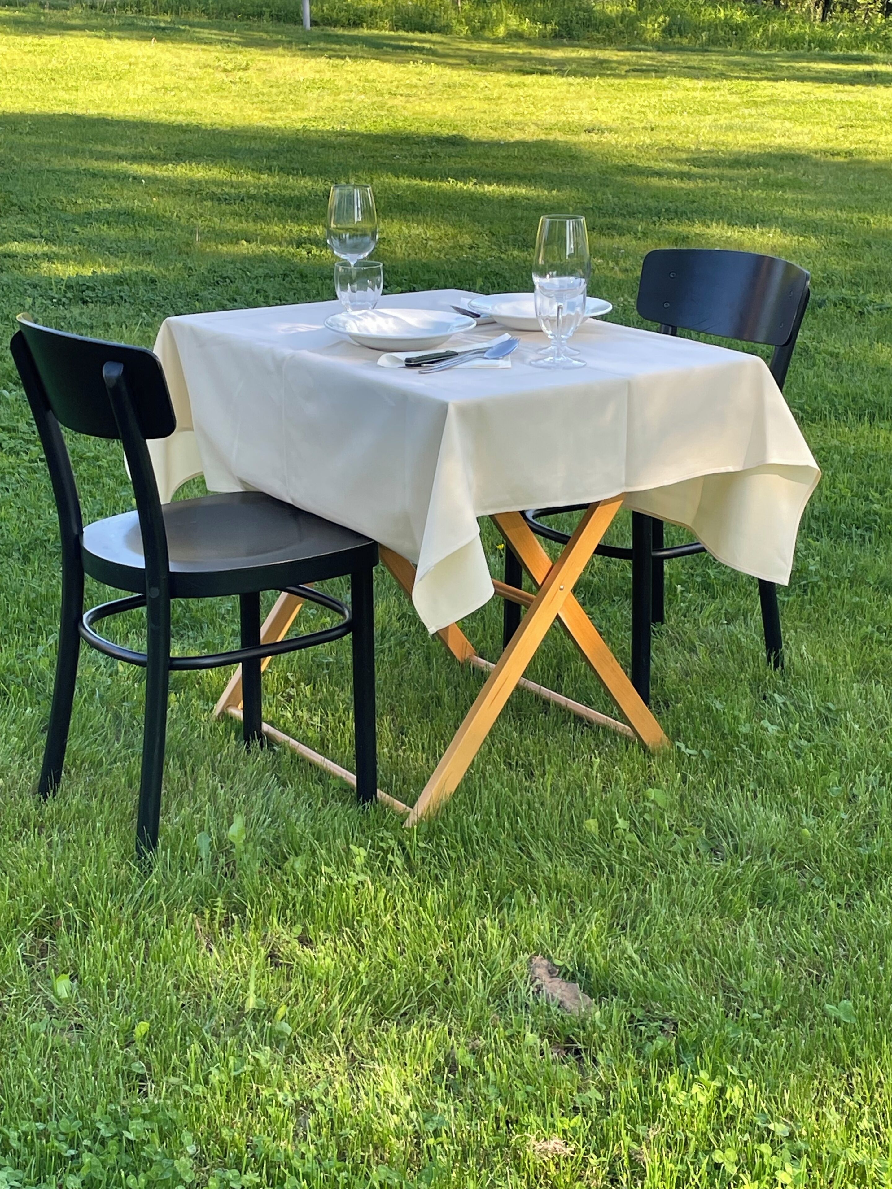 Mesa al aire libre con sillas, mantel blanco y copas de vino vacías.