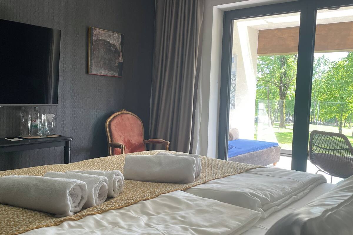 A hotel room with a bed, a chair, a television, and a view of the outdoors.