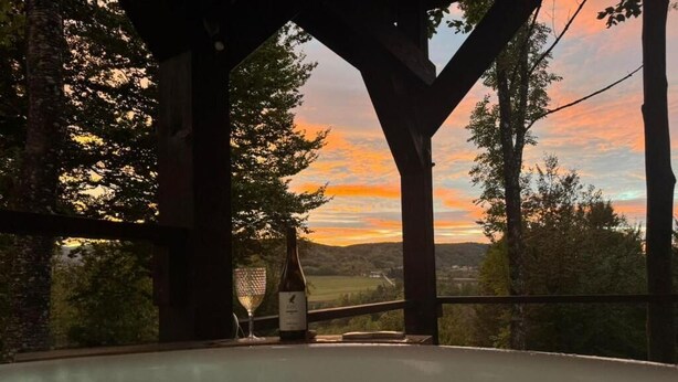 Un jacuzzi bajo una pérgola de madera con vistas a un paisaje al atardecer.