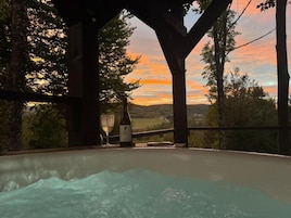 A hot tub under a wooden pergola with a view of a sunset over a landscape.