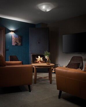 A modern living room with a fireplace, two leather sofas, a coffee table, and a flat-screen TV mounted on the wall. - Equilibrium Villa Relais Plitvice (Rakovica)
