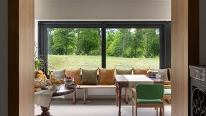 A modern living room with a large window, a wooden table, a green chair, and a sofa with cushions. - Equilibrium Villa Relais Plitvice (Rakovica)