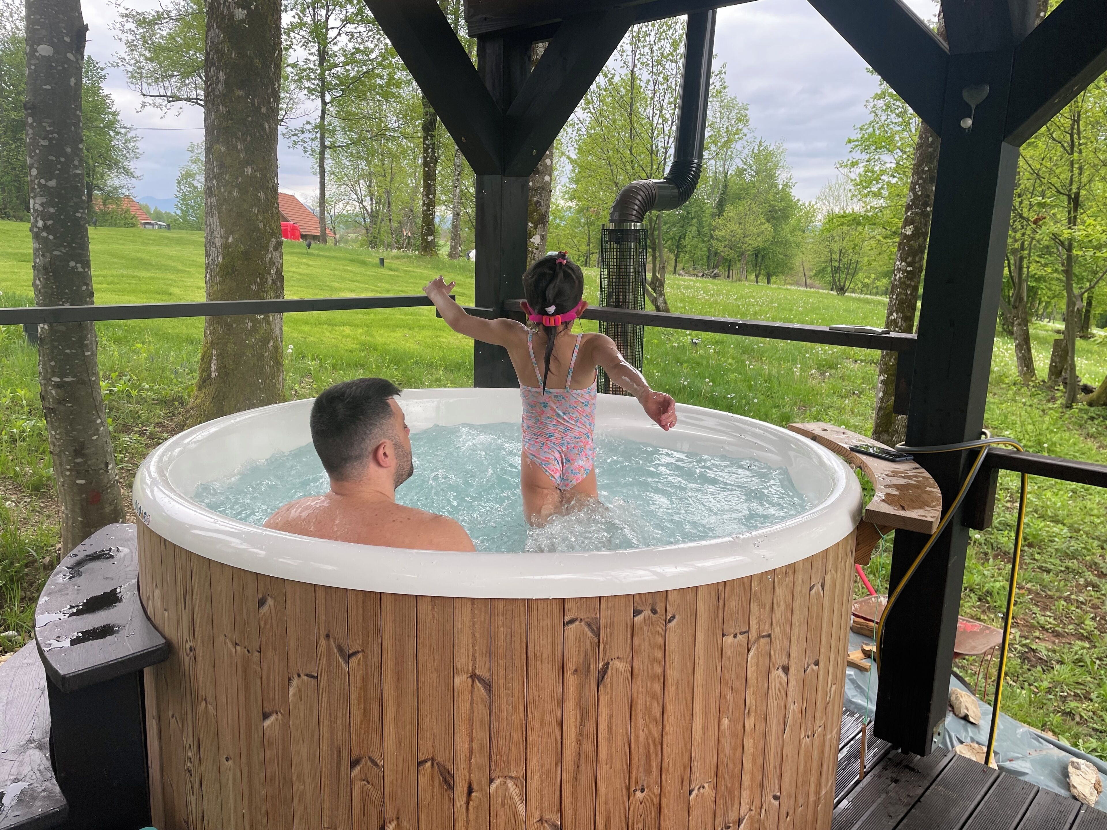 Un jacuzzi con revestimiento de madera, rodeado por una terraza de madera y árboles.