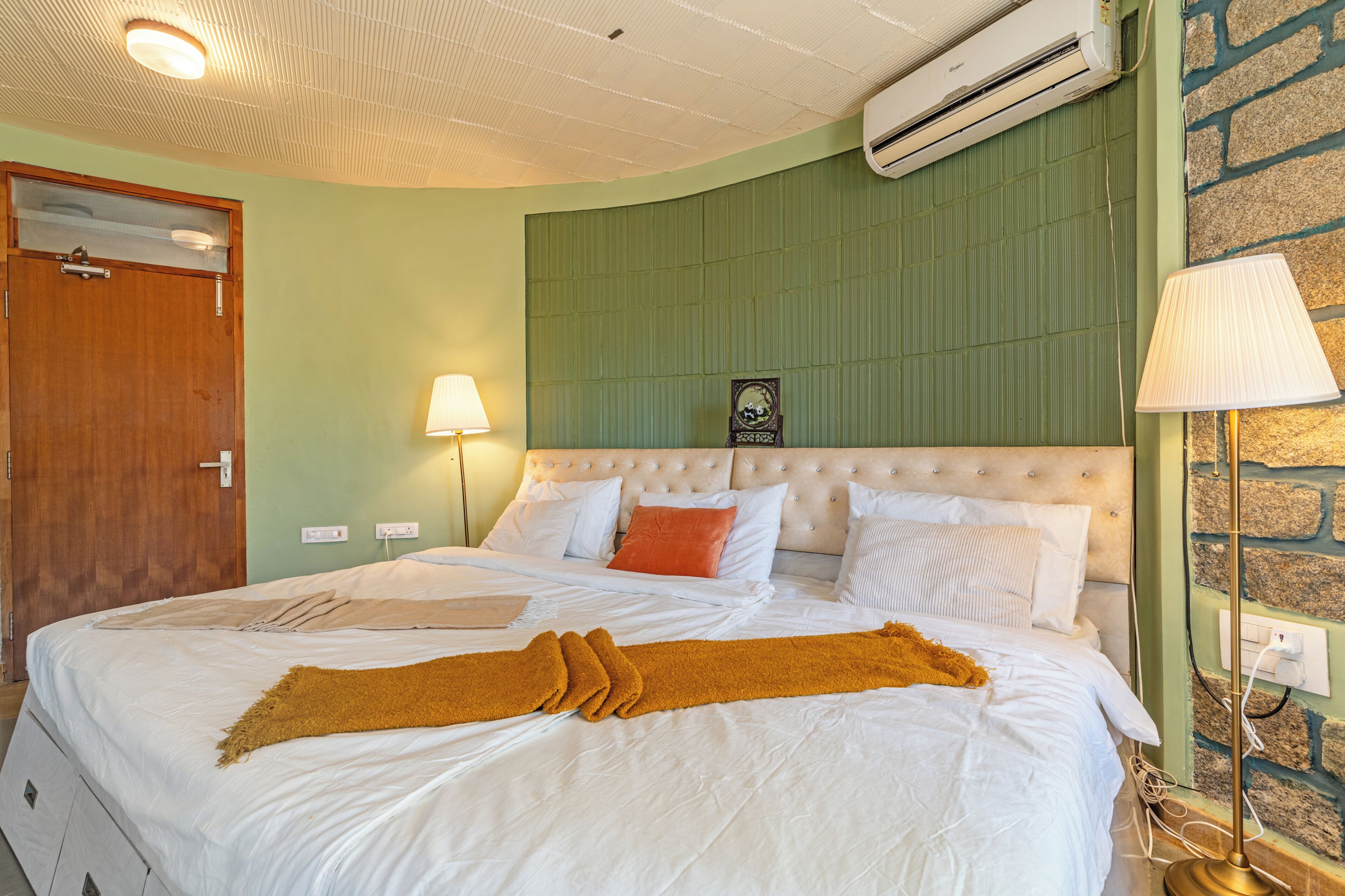 Une chambre d’hôtel avec un lit, une porte en bois, un climatiseur et une lampe.