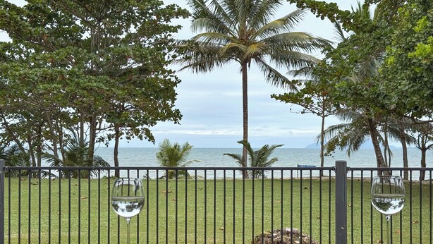 Un balcon avec vue sur la mer, des palmiers et deux verres à vin posés sur la rambarde.