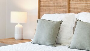Un lit bien fait, avec une literie blanche et deux oreillers, une lampe de chevet et une tête de lit en osier.