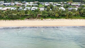 Vue aérienne d’une zone résidentielle côtière, avec des maisons, des palmiers et une plage de sable.