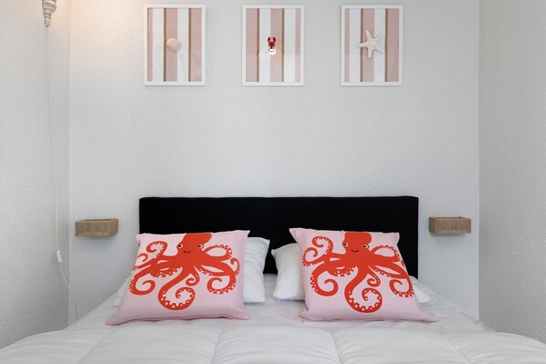 Una cama con dos almohadones de pulpo, un cabecero negro y tres lámparas fijadas a la pared.