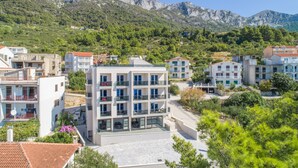 Un edificio moderno con varios balcones, rodeado de vegetación y montañas.