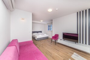 A modern room with a bed, a pink sofa, a TV, and a wooden floor. - Altiora Prestige Residence 205 (Gradac)