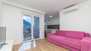 A modern living room with a pink sofa, a flat-screen TV, and a sliding glass door leading to a balcony. - Altiora Prestige Residence 205 (Gradac)