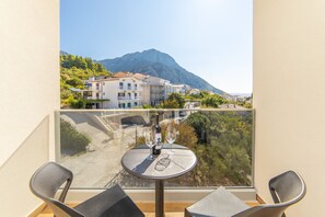 A balcony with a table, two chairs, and a view of buildings and mountains. - Altiora Prestige Residence 205 (Gradac)